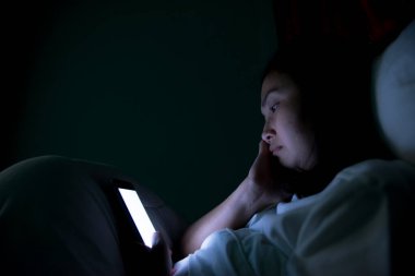 Asyalı kadın gece yatakta akıllı telefonla oyun oynuyor, Taylandlılar, sosyal medya bağımlısı.