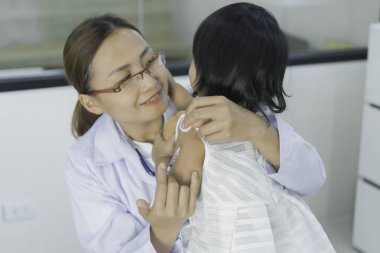 Solunumunu ve kalbini kontrol etmek için steteskop kullanan Asyalı bir doktor, Taylandlı çocukların sağlığını kontrol ediyor.