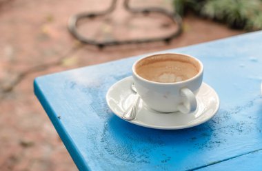 Mavi ahşap masada beyaz fincan kahve.