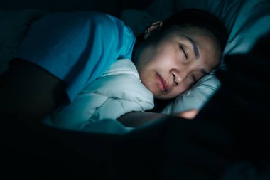 Asyalı kadın gece yatakta akıllı telefon oynar, Taylandlılar, sosyal medya bağımlısı, bütün gece internet oynar, Lychnobite