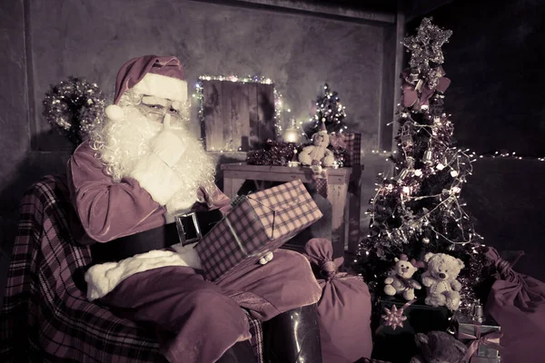 圣诞老人在家里拿着礼品盒 坐在椅子上想着给孩子送礼物盒的计划 — 图库照片