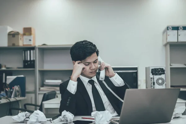 Businessman stress from hard work on the desk at office dark tone.take with boss on telephone,thailand people