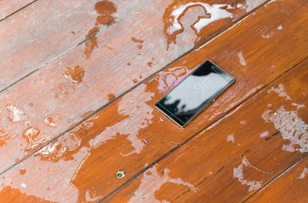 mobile phone with water drops on wet wooden background