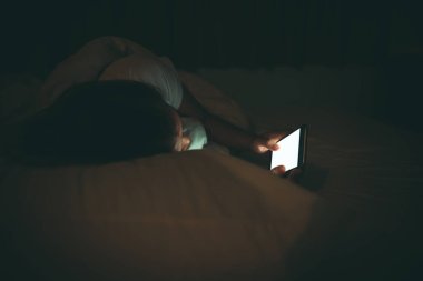 Asyalı kadın gece yatakta akıllı telefonla oyun oynuyor, Taylandlılar, sosyal medya bağımlısı.