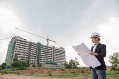 Genç Asyalı mühendis binanın kağıt planını arıyor.