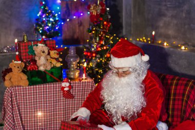 Noel baba holding hediye evde kutusunda, gönderilen hediye kutusu plan vermek çocuklar için sandalye düşünmek oturmak