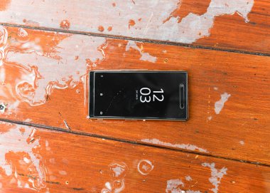 Islak ahşap arka planda su damlaları olan cep telefonu