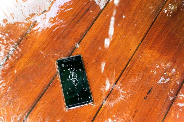 mobile phone with water drops on wet wooden background