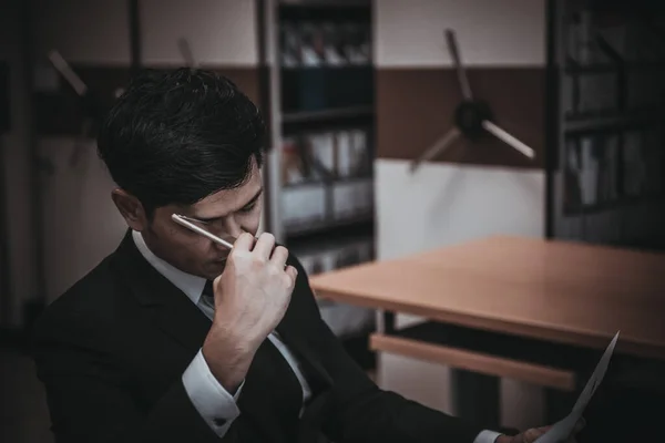 Asian businessman in black suit think idea for work at office,he work overtime alone in a company,dark tone,thailand people