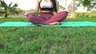 Asyalı genç bir kadın gündüz vakti parkta yoga yapıyor.