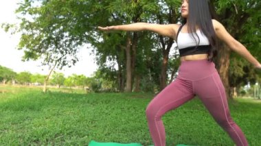 Asyalı genç bir kadın gündüz vakti parkta yoga yapıyor.