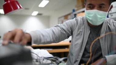 Koruma maskesindeki teknisyen depodaki stokları kontrol ediyor. Laboratuvardaki mühendislik ekipmanları sayıyor. 
