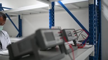 Koruma maskesindeki teknisyen depodaki stokları kontrol ediyor. Laboratuvardaki mühendislik ekipmanları sayıyor. 