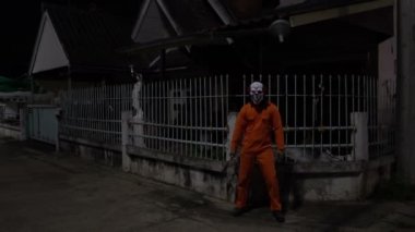 Gece olay yerinde silahlı bir palyaço maskesi takan Asyalı adam Cadılar Bayramı festivali konsepti turuncu kıyafetli bir katilin korkunç fotoğrafı.