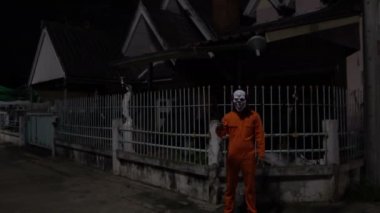 Gece olay yerinde silahlı bir palyaço maskesi takan Asyalı adam Cadılar Bayramı festivali konsepti turuncu kıyafetli bir katilin korkunç fotoğrafı.