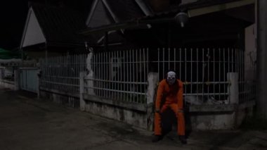 Gece olay yerinde silahlı bir palyaço maskesi takan Asyalı adam Cadılar Bayramı festivali konsepti turuncu kıyafetli bir katilin korkunç fotoğrafı.