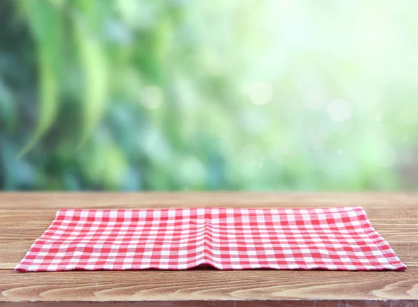 Red checkered picnic cloth on wooden tablue blurred green backgr — Stock Photo, Image