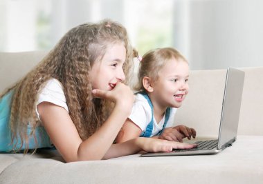 Çocuklar dizüstü bilgisayar kullanır. Çocuklar internet videoları izler. Küçük kızlar kanepede yatar ve ekrana bakarlar. Çevrimiçi çocukluk yaşam tarzı.