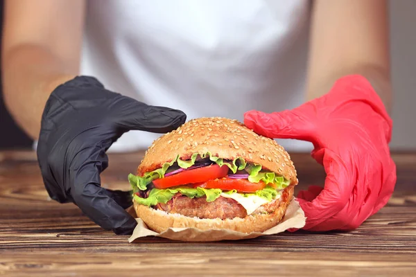 Hamburger in hands, person eating burger in gloves.Sandwich on wooden table.Fast food or junk food.