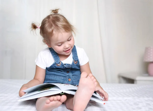 子供は本を屋内で読んでいます 白人の子供はベッドの上に座って本を読みます — ストック写真