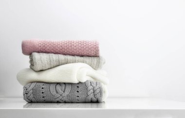 Yumuşak renkler örülmüş giysiler beyaz masa boş arkaplan üzerine yığılır. Kaşmir istiflenmiş tekstil. Kış katlanmış kazak yığını.