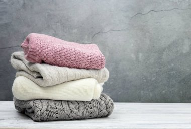 Bir yığın örgü kıyafet, katlanmış süveterler gri boş arka planda yığılıyor. Kış örgü öbekleri, hiç kimse. El yapımı giysiler üst üste yığılıyor..