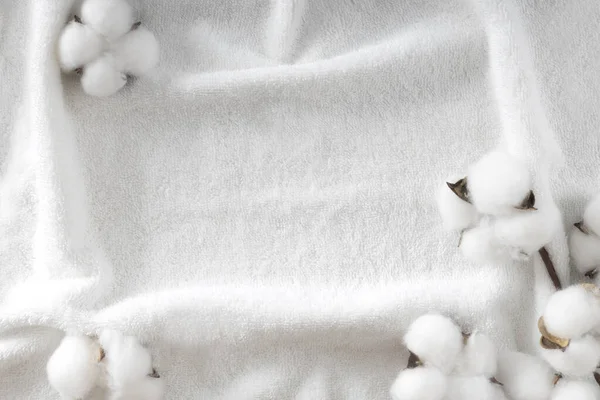Pamuk çiçeği tomurcuğuyla dekore edilmiş beyaz havlu dokusu. Kozmetik arka planı, spa arka planı. Banyo ögeleri gösteriliyor. Boş kopya alanı çerçevesi.
