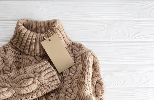 Kahverengi örülmüş, beyaz ahşap arka planda boş etiketli yün bir kazak. Bilgi etiketli kazan.