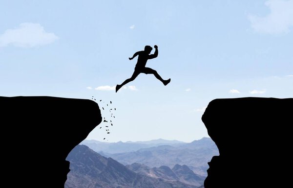 Man jumping over abyss in front of mountain background.