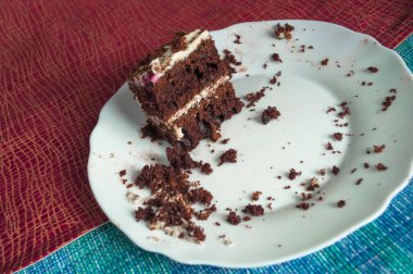 Beyaz bir tabakta kremalı son parça çikolatalı kek, masa örtüsünde kırıntılar olan çok renkli süslemelerle süslenir.