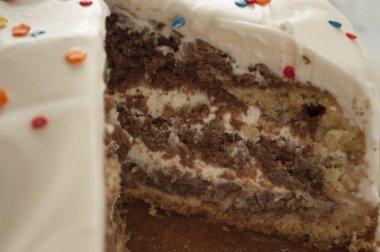 Çok renkli süslemelerle süslenmiş kremalı çikolatalı kek. Kesilmiş bir parça, makro fotoğraflı bir pasta.