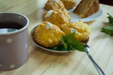 Krem şantiyle dolu eklerlerin bir kısmı ahşap arka planda bir fincan çayla. Muhallebi kurabiyesi ve çay. Bir tabakta ekler ve yanlarında beyaz daireler çizen siyah bir fincan.. 