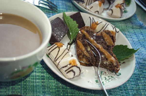 Naneli, şekerli, karamelli ve pudra şekerli çikolatalı turta ve mavi masa örtüsü üzerinde süt olan bir fincan kahve.