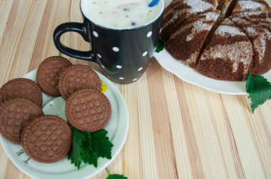 Porsiyon çikolatalı kurabiyeler, turta ve ahşap arka planda böğürtlenli bir fincan yoğurt. Çikolata parçacıklı kurabiyeler. Tabakta çikolatalı kurabiye ve yanlarında siyah bir fincan beyaz daireler çiziyor..