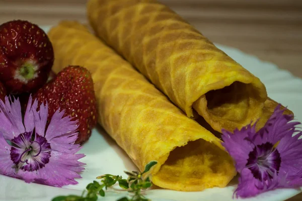 Waffle tubes, strawberries and carnation flowers . Composition on a light wooden background decorated with carnation  flowers