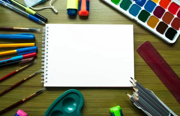Öğrenci kırtasiyesi ve ahşap arka planda beyaz eskiz defteri kağıdı ile eğitim modeli, üst görüş. Çizim seti. Eğitim kavramı
