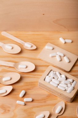 Tahta kutuda beyaz vitamin hapları ve tahta arka planda tahta kaşıklar. Sağlığınızı ve bağışıklık sisteminizi korumak için vitaminler, mineraller ve gıda takviyeleri. Beyaz tabletler üst görünüm.