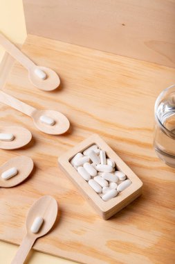 Tahta kutuda beyaz vitamin hapları ve tahta arka planda tahta kaşıklar. Sağlığınızı ve bağışıklık sisteminizi korumak için vitaminler, mineraller ve gıda takviyeleri. Beyaz haplar