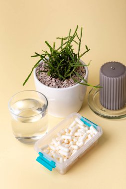 Vitaminler, mineraller ve bir bardak su, gri mum ve ev bitkisi sarısı arka planda beslenme malzemeleri. Bir sürü beyaz hap, tablet, kapsül ve gıda takviyesi. Sağlıklı yaşam tarzı