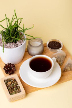 Bir fincan siyah çay, ev yapımı rhipsalis, mum ve çay yaprakları bej arka planda güzel bir kompozisyon. Çay zamanı. Lezzetli sıcak çay. Sıcak atmosfer.