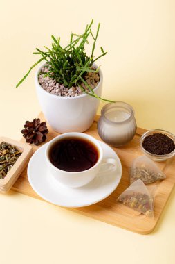 Bir fincan siyah çay, ev yapımı rhipsalis, mum ve çay yaprakları yukarıdan bej arka planda güzel bir kompozisyon. Çay zamanı. Lezzetli sıcak çay. Sıcak atmosfer.