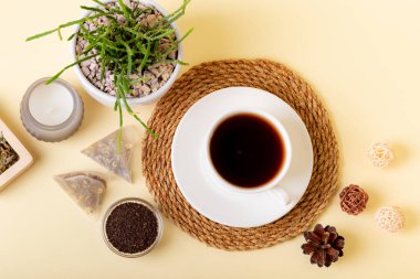 Bir fincan siyah çay, ev yapımı rhipsalis, mum ve çay yaprakları yukarıdan bej arka planda güzel bir kompozisyon. Çay zamanı. Lezzetli sıcak çay. Sıcak atmosfer.