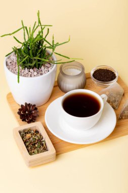 Bir fincan siyah çay, ev yapımı rhipsalis, mum ve çay yaprakları bej arka planda güzel bir kompozisyon. Çay zamanı. Lezzetli sıcak çay. Sıcak atmosfer.