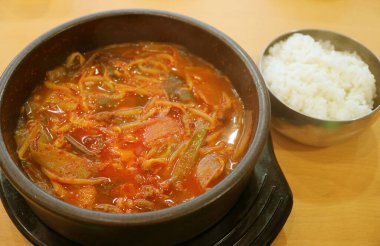 Bir kap Kimchi Jjigae ya da Kore Sıcak ve Baharatlı Kimchi Güveci Tahta Masa üzerinde bir kase Pirinç ile servis edilir.