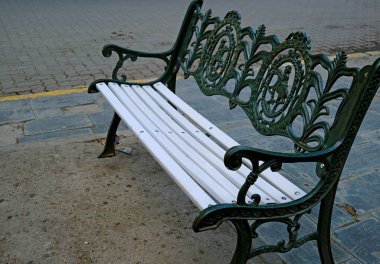 Koyu yeşil işlemeli, boş beyaz ahşap. Meydanda demir işlemeli bir bank.