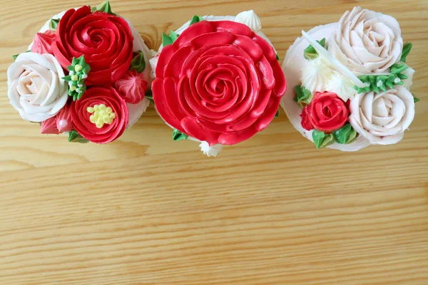 木製のテーブルに隔離された見事な花の形をした霜降りで飾られた3つのカップケーキのトップビュー — ストック写真