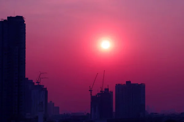 Pop art style purple pink colored sky with dazzling sun rising over the silhouette of construction site