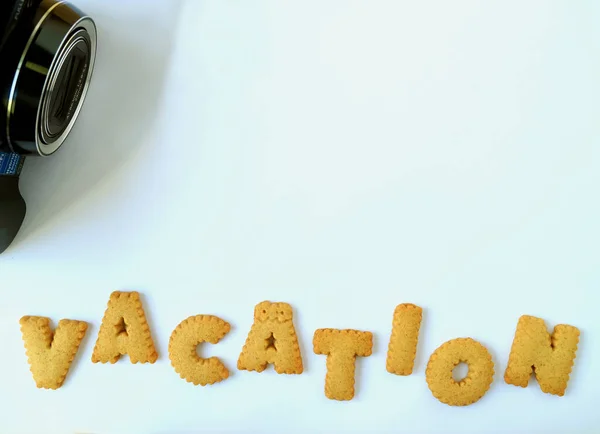 黑色相机的顶视图和 Vacation 这个词 用淡蓝色桌子上的字母表形饼干制成 有文字和设计的自由空间 — 图库照片