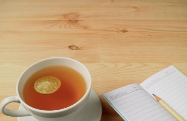 Bir fincan sıcak limon çayı ve doğal renk ahşap masa üzerine kalemli Lined Note kağıtları, metin ve tasarım için boş alan