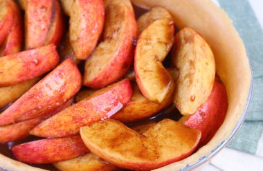 Esmer şeker ve baharatlarla karıştırılmış taze elma dilimleri hamurdan yapılmış turta tabağına konur.